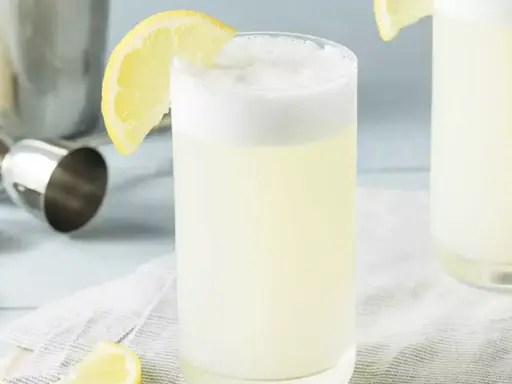 Un verre de gin fizz, garni d'une tranche de citron, prêt à être dégusté. Une recette rafraîchissante pour l'été.