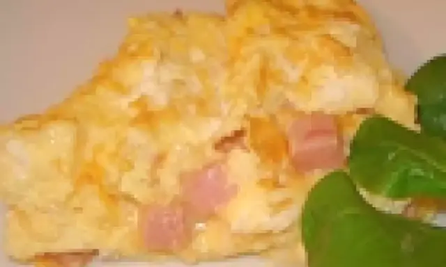 Une omelette jambon fromage dorée, garnie de dés de jambon rose et de fromage fondant, accompagnée de quelques feuilles vertes.