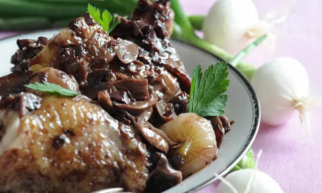 Un plat de coq au vin savoureux, avec des morceaux de poulet tendres, des champignons et des oignons dans une sauce riche.