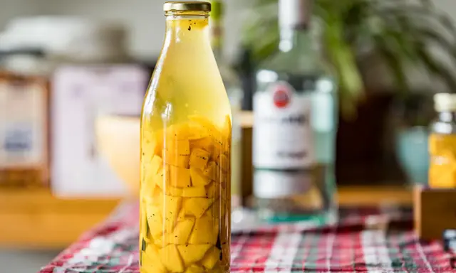 Bouteille de rhum arrangé mangue, avec des morceaux de fruits jaunes et des épices.