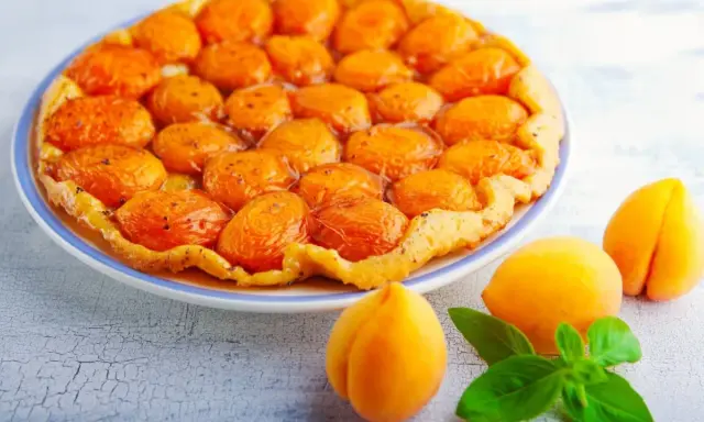 Découvrez les meilleures tartes aux fruits : une tarte tatin aux abricots dorés et caramélisés, garnie de fruits frais et de feuilles de basilic.