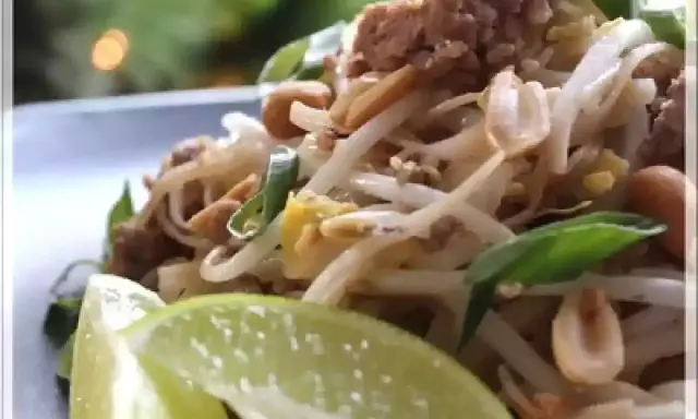Délicieux pad thai porc avec pousses de soja, cacahuètes et quartiers de citron vert.