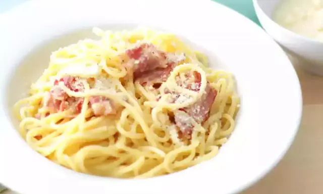 Une assiette de spaghetti crémeux, parsemée de lardons et de parmesan. La vraie recette carbonara italienne, un délice simple et authentique.