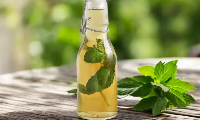 Une bouteille de sirop de menthe maison, avec des feuilles de menthe fraîche à côté, sur une table en bois.