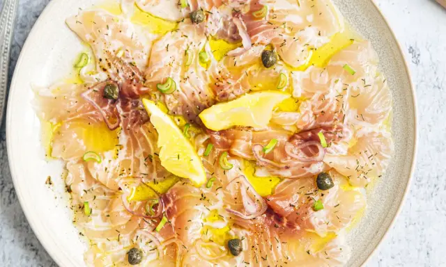 Délicieux carpaccio de saumon, fines tranches de poisson cru arrosées d'huile d'olive, garnies de câpres, oignons rouges et quartiers de citron.