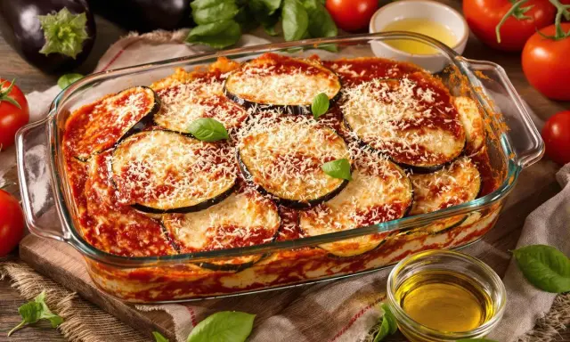 Un plat de parmigiana di melanzane, gratiné et garni de parmesan râpé, prêt à être dégusté. Des aubergines fraîches et des tomates entourent ce délice italien.