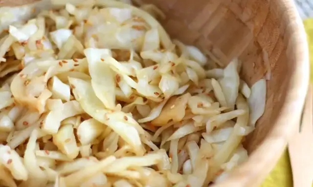 Salade de chou râpé assaisonnée de graines de sésame, servie dans un bol en bois.