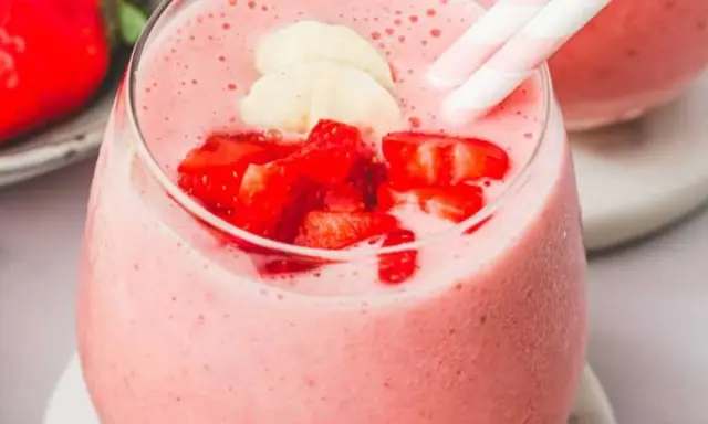 Un délicieux smoothie fraise banane, garni de morceaux de fruits frais et de pailles rayées roses et blanches.