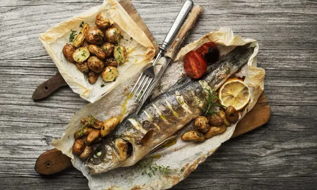 Truite entière cuite en papillote sur un barbecue, accompagnée de pommes de terre rôties et de tomates.