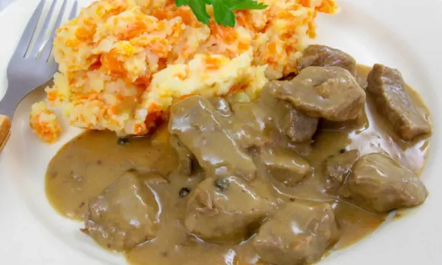 Un plat de rognon de boeuf en sauce, servi avec une purée de pommes de terre et carottes, garni de persil.
