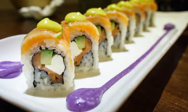 Une délicieuse recette maki original : rouleaux de saumon, avocat, concombre et fromage frais, ornés d'une touche de sauce verte et de purée violette.