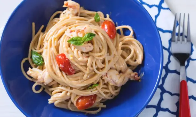 Un plat de pâtes aux crevettes, tomates cerises et basilic, servi dans un bol bleu vif. Un délice !