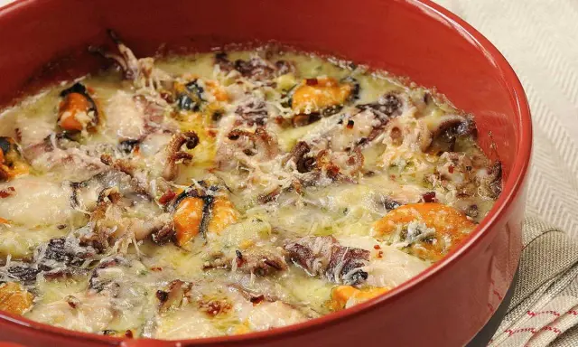 Un délicieux gratin de poisson et fruits de mer, gratiné au fromage, dans un plat rouge.