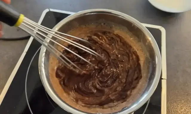 Préparation d'une recette ganache chocolat : du chocolat fondu est fouetté dans une casserole sur une plaque chauffante.