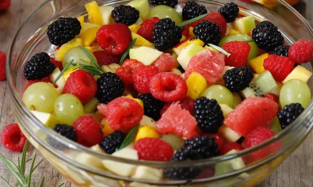 Un bol de salade de fruits frais et colorée, garnie de framboises, mûres, raisins verts, morceaux de pomme, pamplemousse et kiwi.