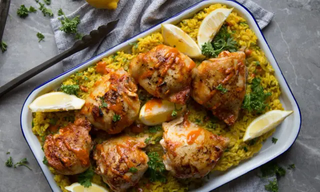 Poulet piri piri savoureux sur un lit de riz jaune, garni de quartiers de citron et de persil frais. Un délice épicé à partager.
