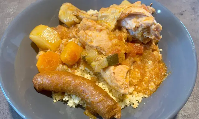 Un plat appétissant de tajine poulet merguez, servi sur un lit de semoule, avec des morceaux de poulet, des légumes et une merguez dorée.