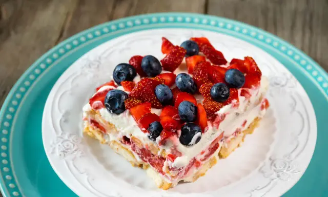 Tranche de tiramisu aux fruits rouges, garnie de fraises et myrtilles fraîches. Un délice estival.