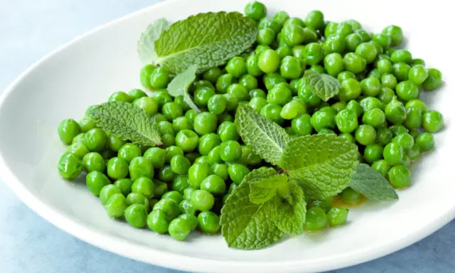 Petits pois frais et menthe sur une assiette blanche, une idée simple pour une recette de petit pois légère et savoureuse.