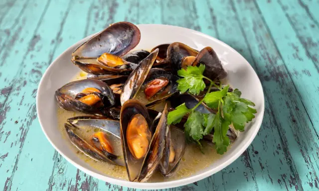 Un plat de moules au roquefort, garni de persil frais, baignant dans une sauce crémeuse.
