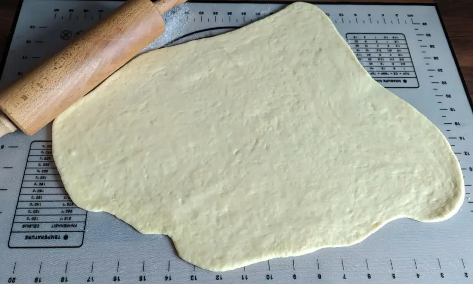 Pâte à beignet légère et croustillante étalée sur un tapis de pâtisserie avec un rouleau à pâtisserie en bois.