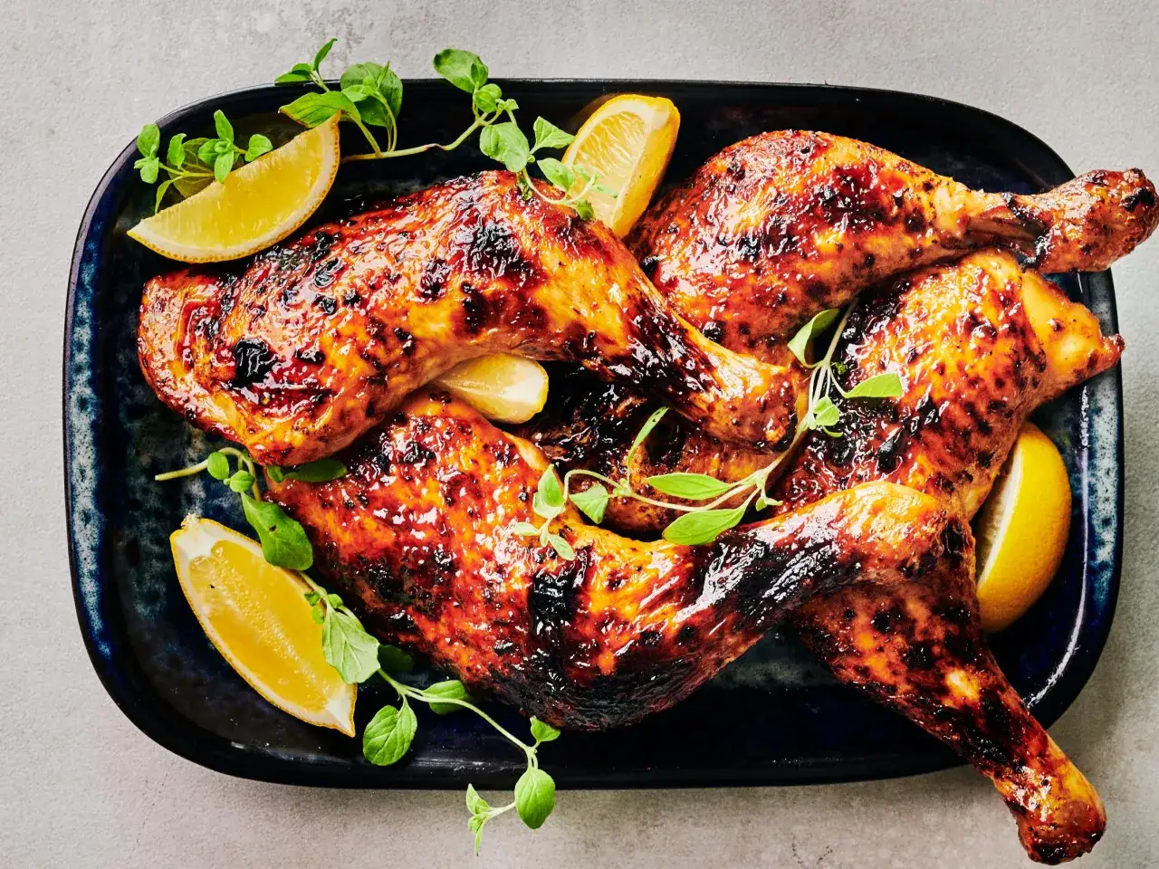 Poulet au miel caram&eacute;lis&eacute;, brillant et app&eacute;tissant, garni de quartiers de citron et de feuilles vertes sur un plat bleu.