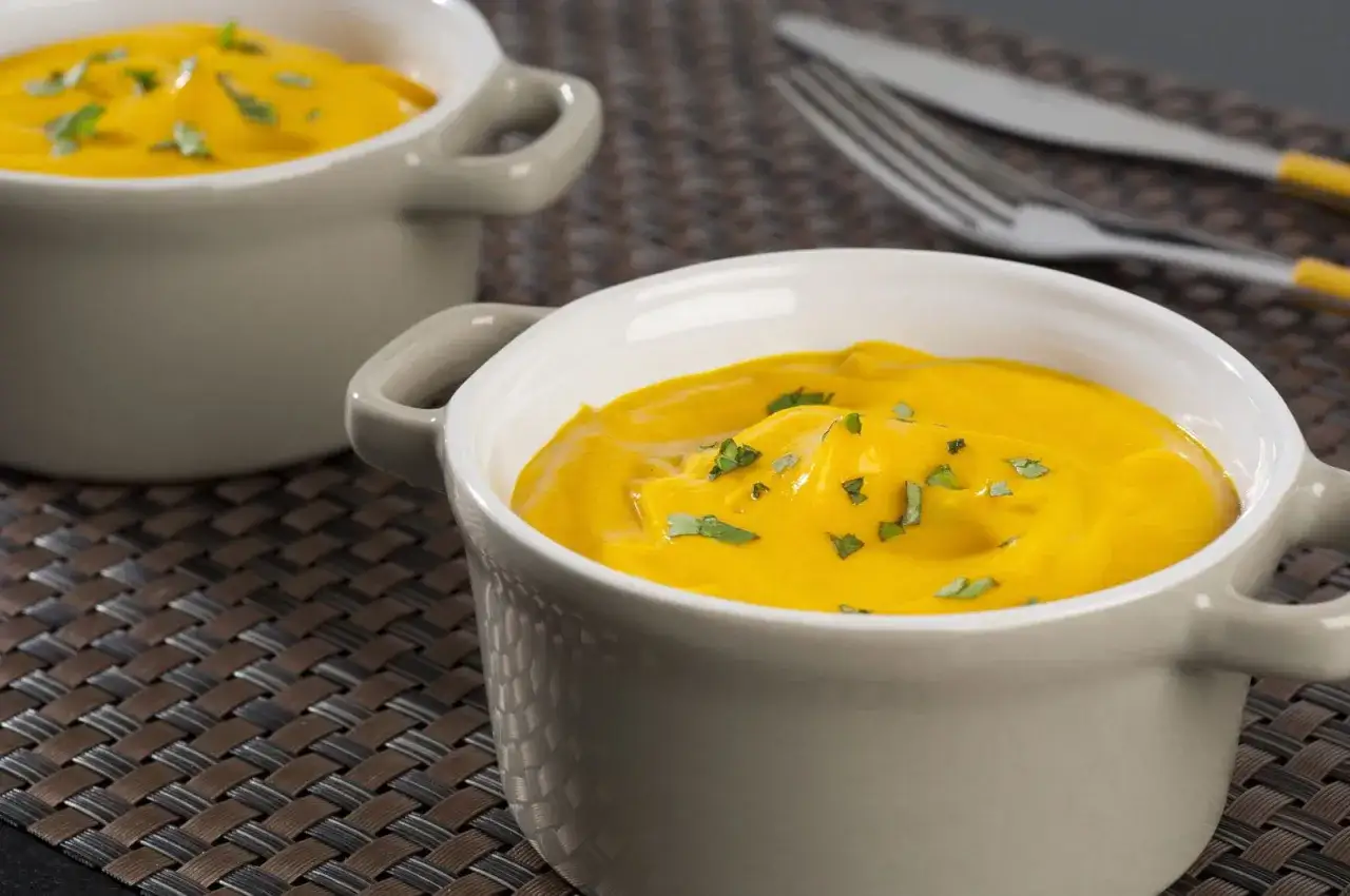 Deux bols de velout&eacute; de pur&eacute;e de carotte, garni de persil frais, sur un set de table tress&eacute;.