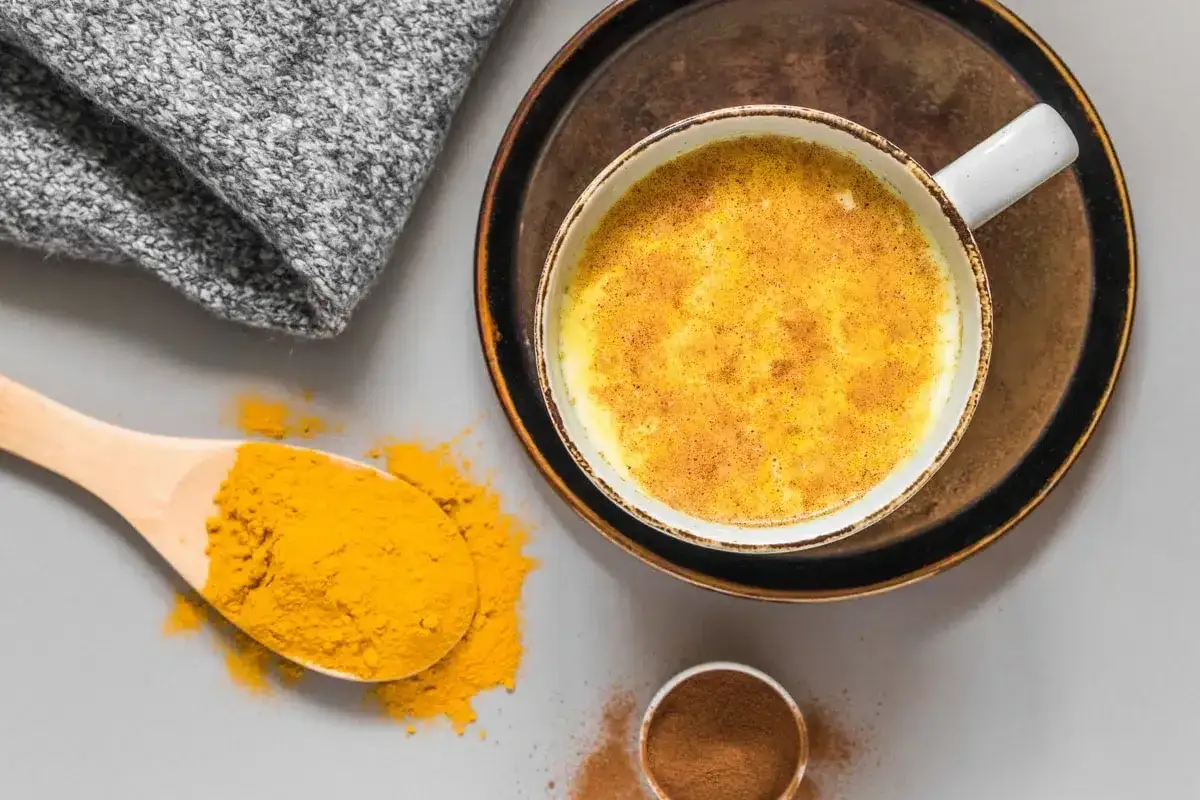 Une tasse de lait au curcuma, avec une cuill&egrave;re de poudre de curcuma et de cannelle &agrave; c&ocirc;t&eacute;.