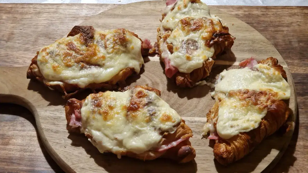 Quatre croissants au jambon gratin&eacute;s, pr&ecirc;ts &agrave; &ecirc;tre d&eacute;gust&eacute;s sur une planche en bois.
