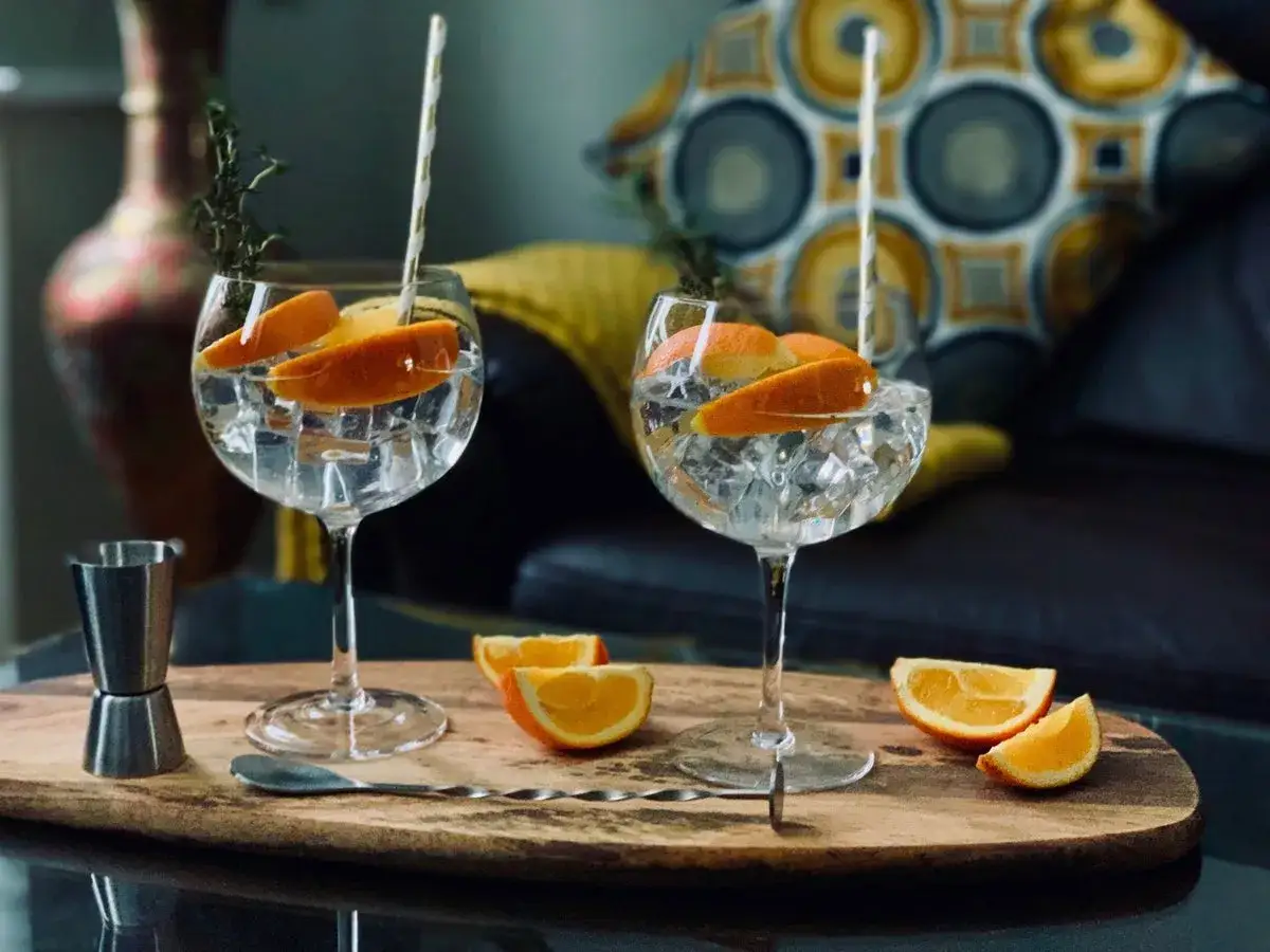 Deux cocktails gin jus de fruit rafra&icirc;chissants, garnis d'orange et de thym, sur un plateau en bois avec des quartiers d'orange.