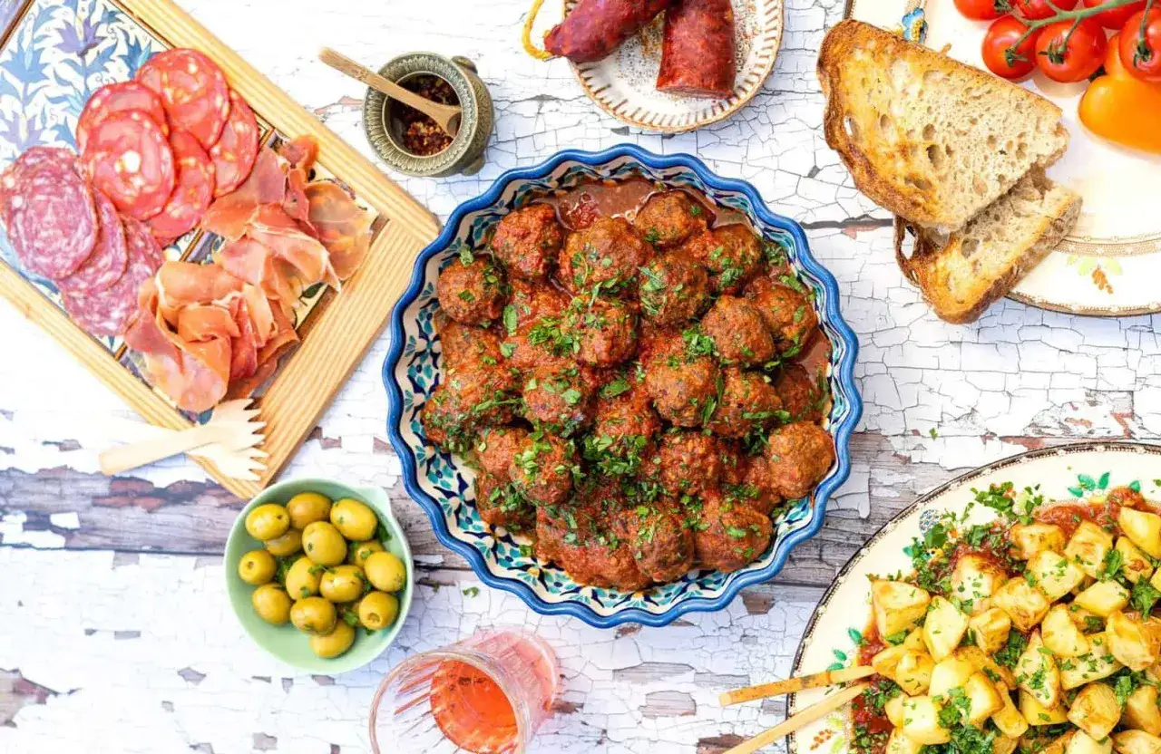 Un plateau de charcuterie, des boulettes de viande sauce tomate, des pommes de terre et des olives, parfait pour une recette tapas gastronomique.