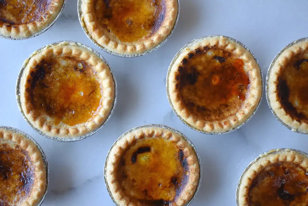 Plusieurs d&eacute;licieux pasteis de nata, aux bords dor&eacute;s et &agrave; la garniture caram&eacute;lis&eacute;e, sont dispos&eacute;s sur une surface claire.